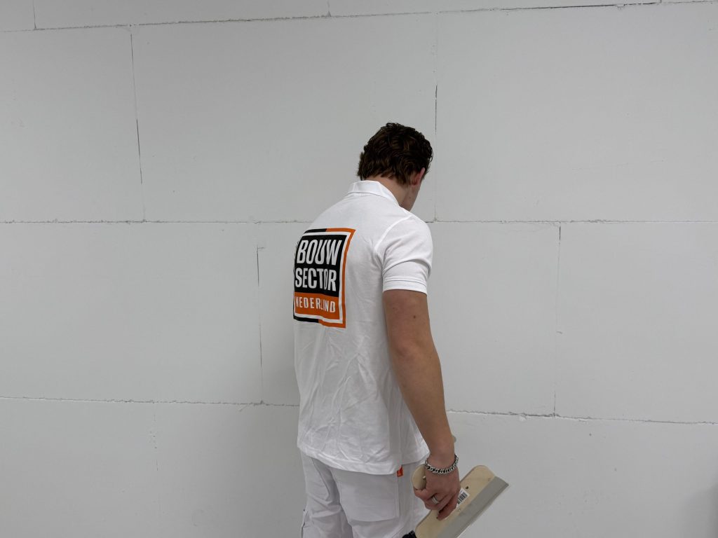 Stukadoor in wit poloshirt van Bouwsector Nederland bekijkt met de spaan in de hand de naden van een muur