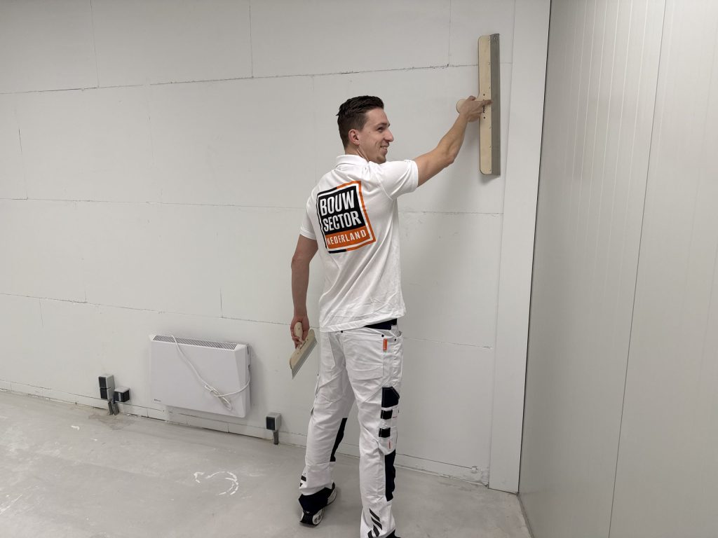 Lachende stukadoor met een lange spaan en een plakspaan aan een grote kale wand